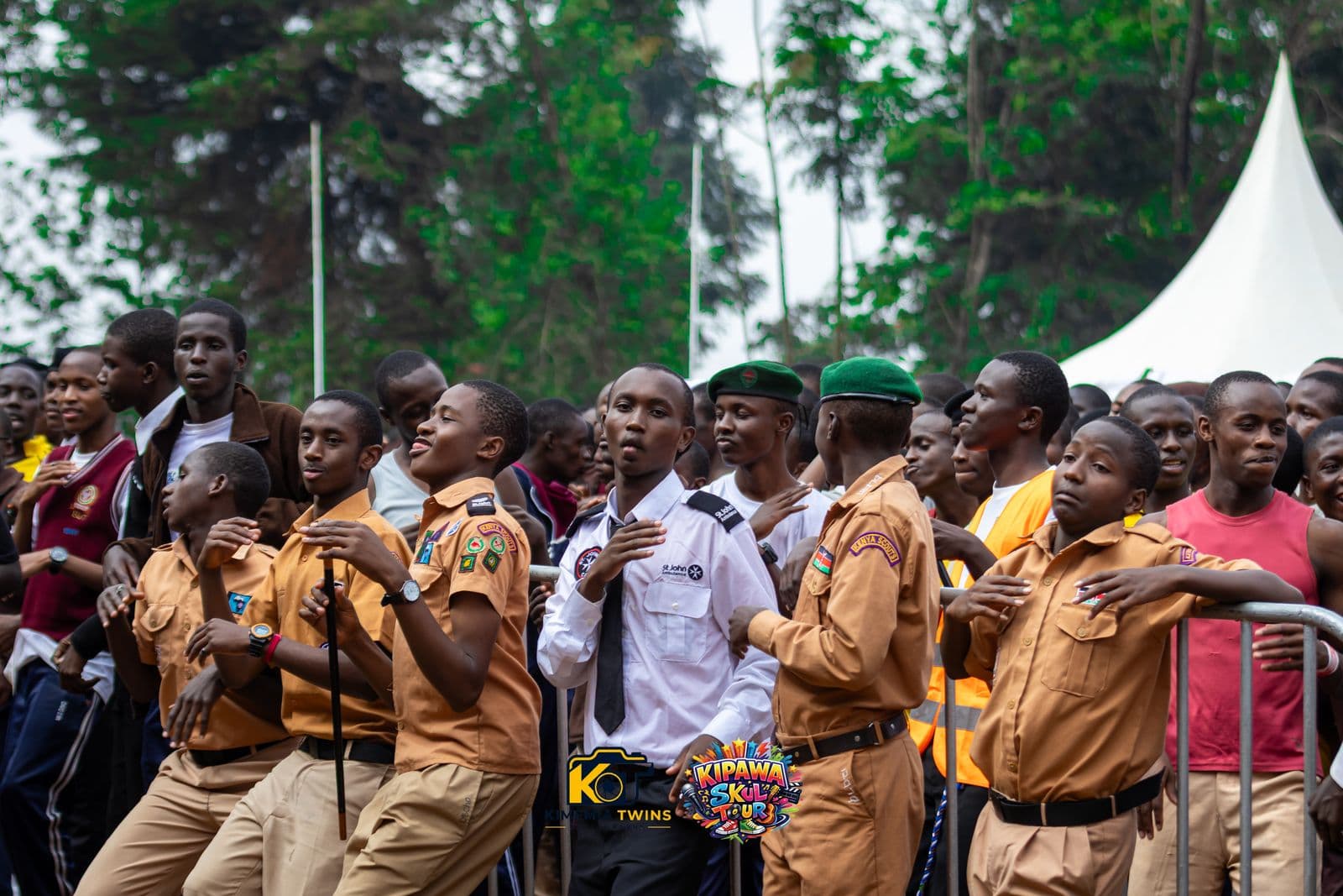Scouts and students watching the Kipawa Skul Tour stage from behind crowd barriers, with an event tent in the background