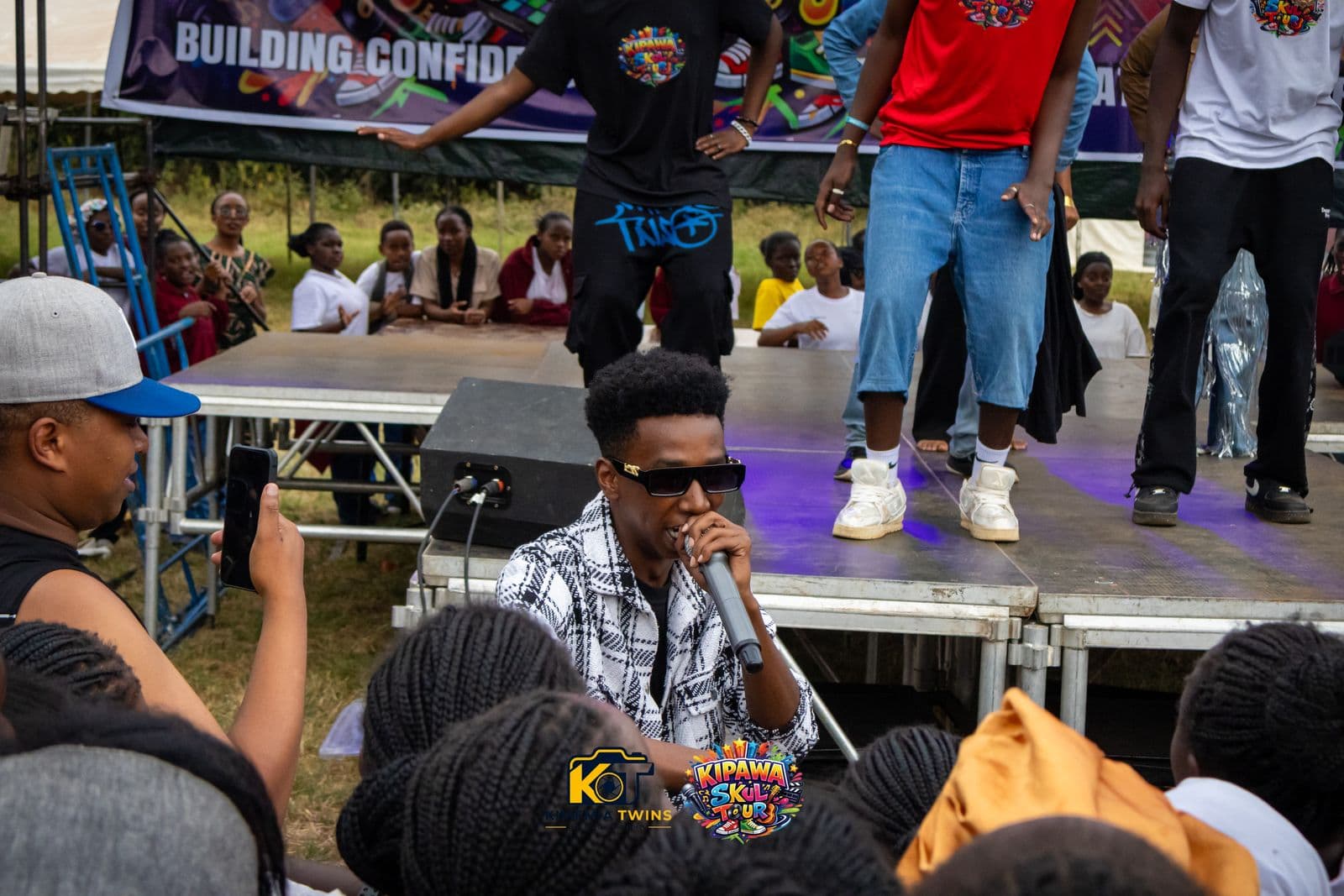 MC with a microphone at the edge of the stage as dancers perform behind him