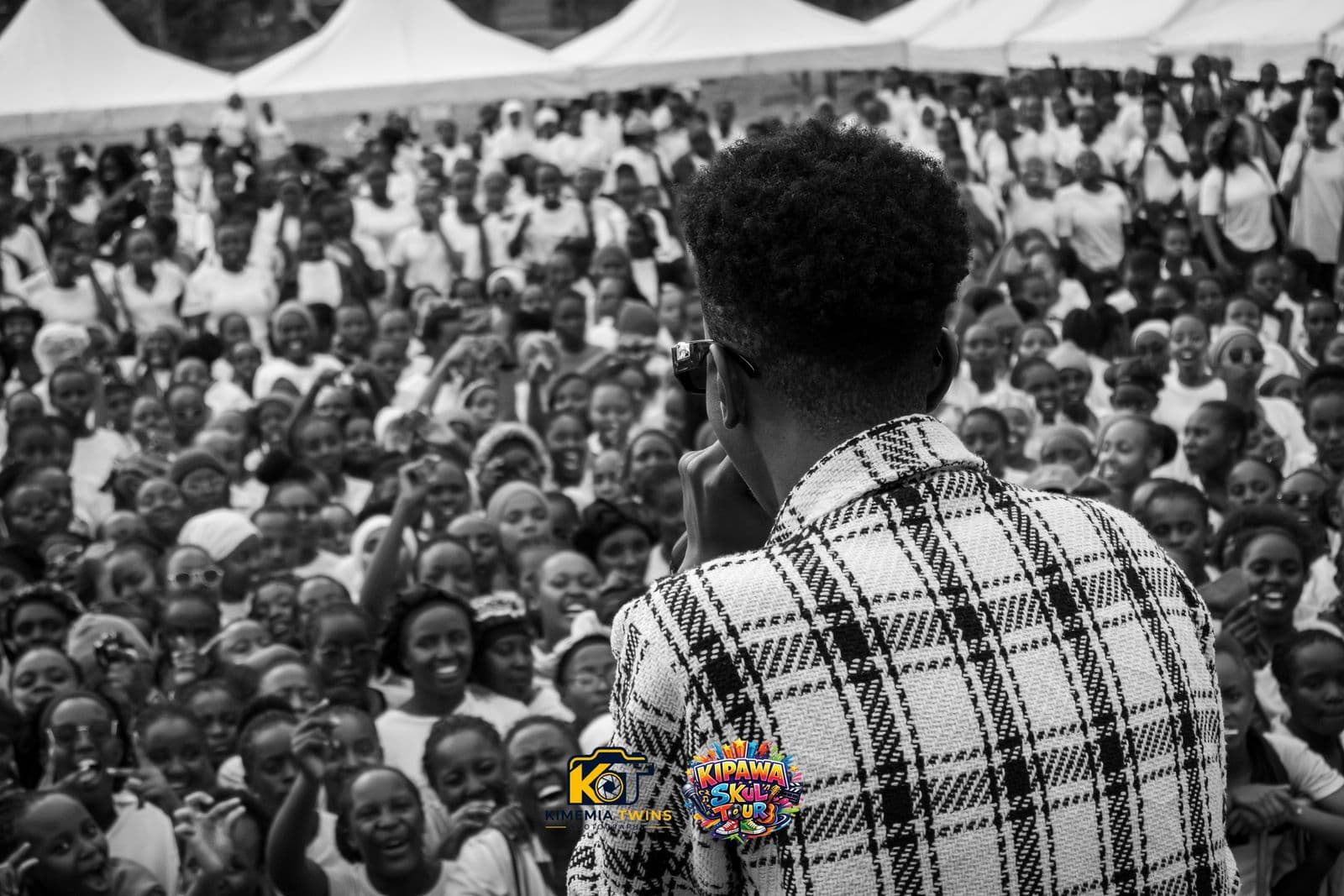 MC facing a huge cheering crowd of students with event tents behind them, black and white photo