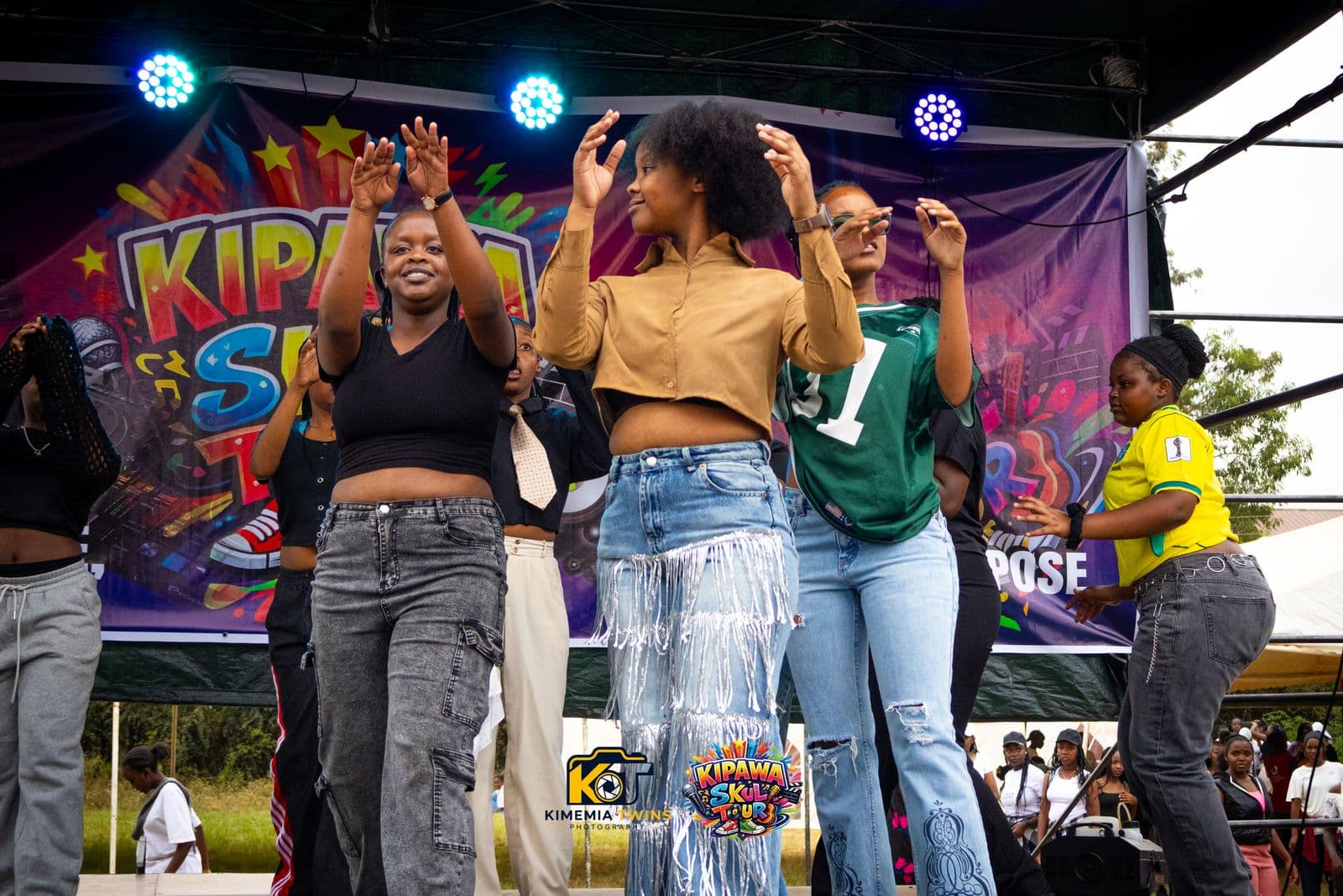 Students dancing with raised hands on stage under blue LED lights