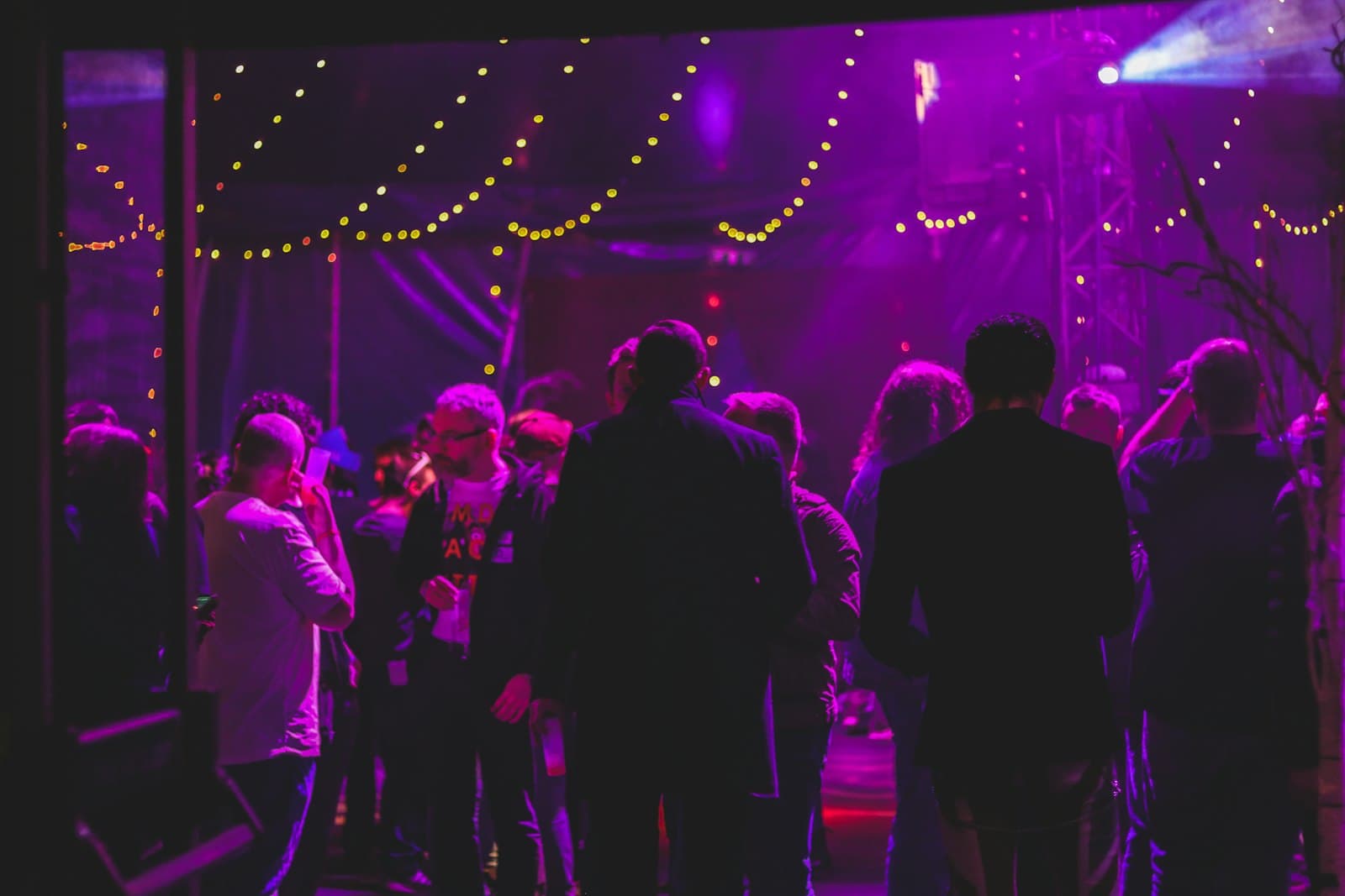 Guests mingling under purple event lighting and warm string lights
