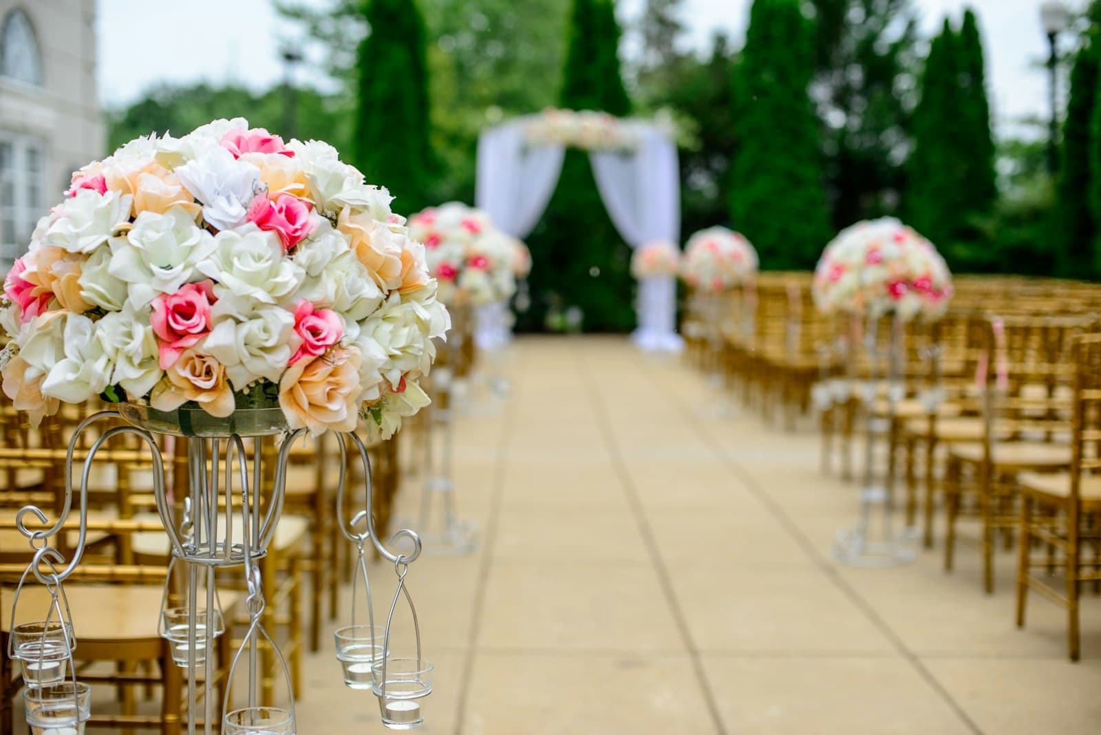 Outdoor event setup with gold chairs, floral stands, and a draped ceremony arch